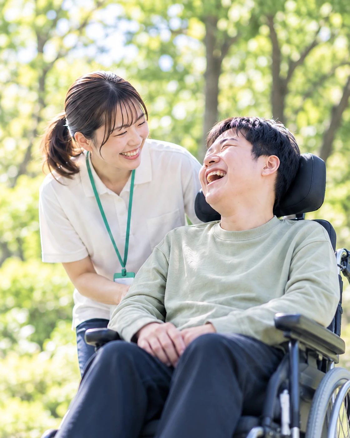 木漏れ日のなか笑顔で過ごす車椅子の男性と支援スタッフ